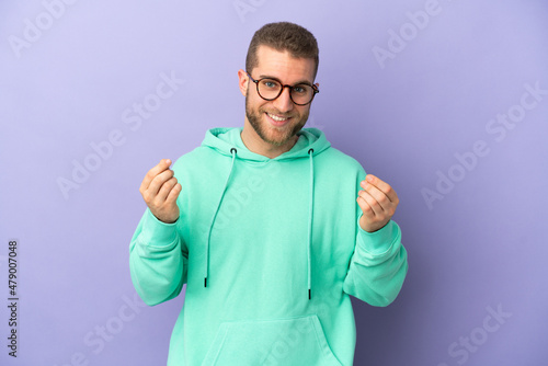 Young handsome caucasian man isolated on purple background making money gesture © luismolinero