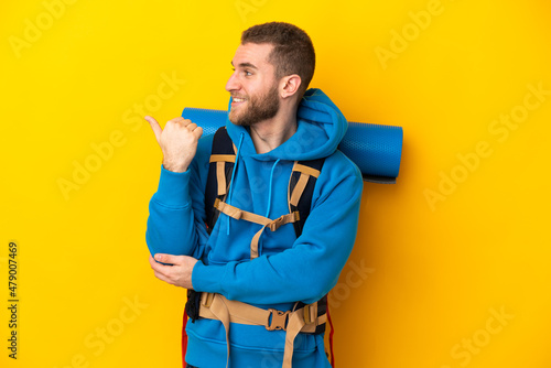 Young caucasian mountaineer man with a big backpack isolated on yellow background pointing to the side to present a product