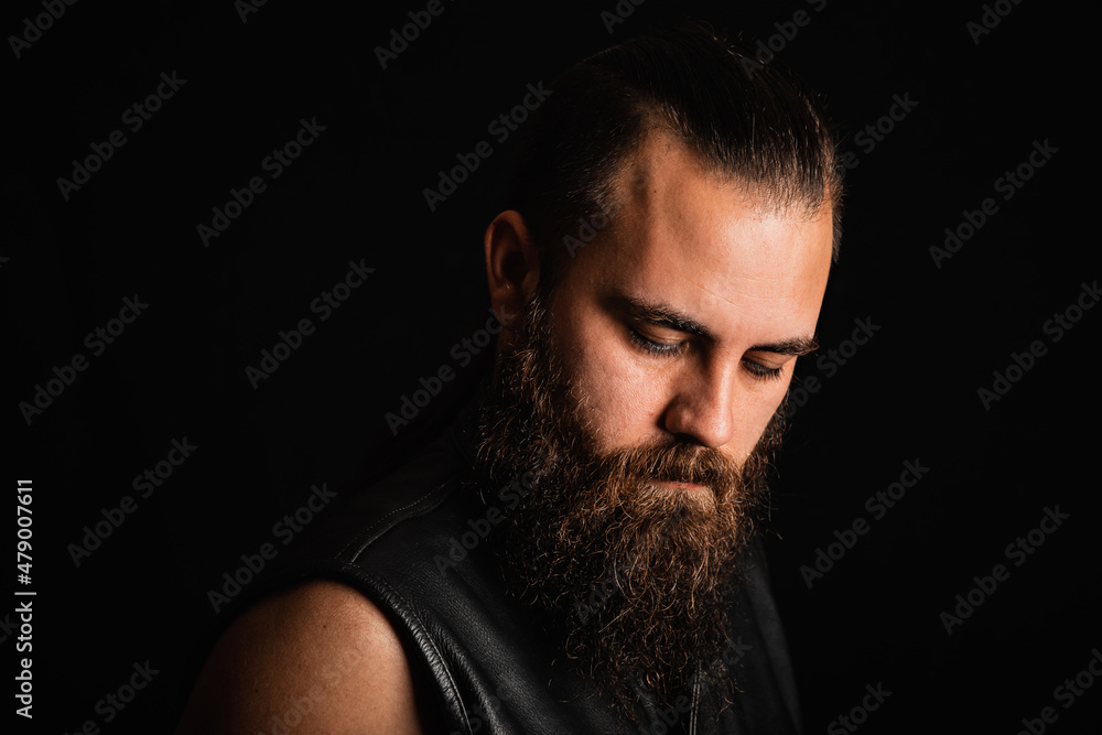 Portrait of a bearded biker man in a black leather vest, looking down in depression and despair Portrait of a bearded biker man in a black leather vest, looking down in depression and despair