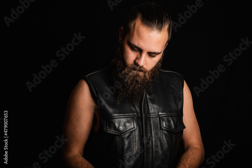 Portrait of a bearded biker man in a black leather vest, looking down in depression and despair