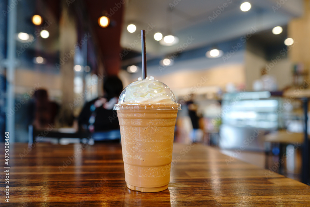A plastic glass of cocoa Frappe or Cocoa shake with brown Straws and Whipped cream put on wooden table A plastic glass of cocoa Frappe or Cocoa shake with brown Straws and Whipped cream put on wooden table