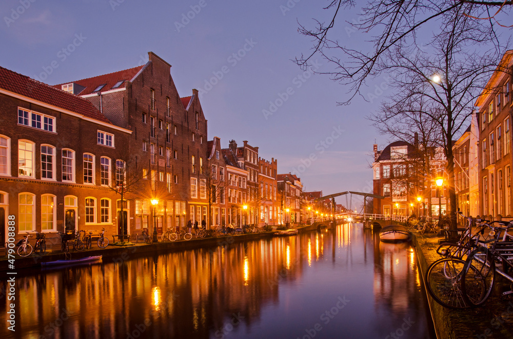 Leiden, The Netherlands, December 16, 2021: view along Oude Rijn canal (the Old Rhine), lined with brick houses, trees and bicycles in the blue hour