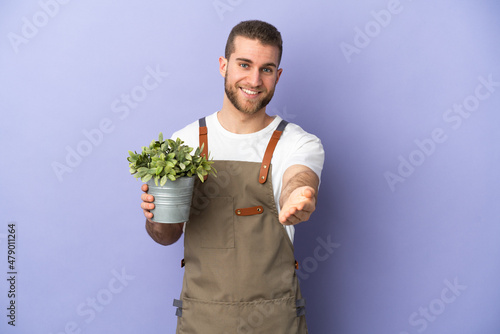 Gardener caucasian man holding a plant isolated on yellow background shaking hands for closing a good deal