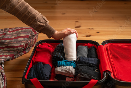 Hands packing a red suitcase with clothes. A hand putting a white folded t-shirt in a suitcase