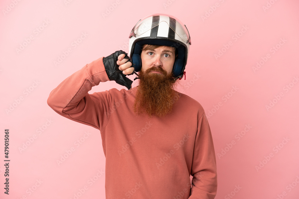 Young reddish caucasian man with a motorcycle helmet isolated on pink background showing thumb down with negative expression Young reddish caucasian man with a motorcycle helmet isolated on pink background showing thumb down with negative expression