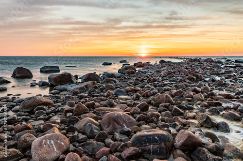 Sun is setting over the rocky pier to calm sea. Romantic view to stones in sea during sunset at Tahkuna, Hiiumaa, Estonia. Coastal rocks, pier, calm blue sea, and colorful sky at dusk photo