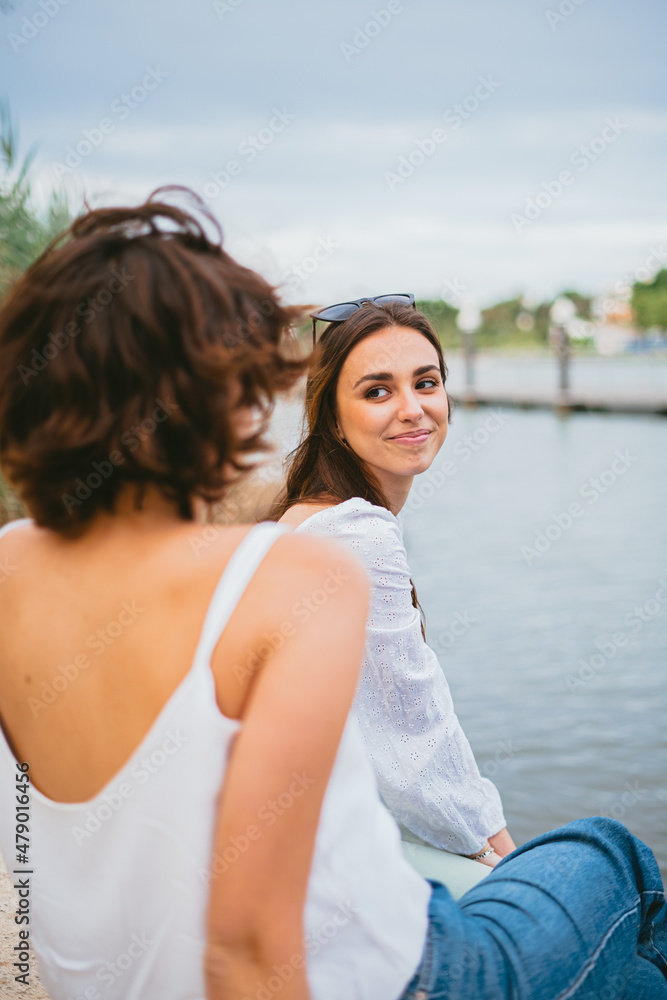 Two young women looking at each other. They are sitting by the river.
