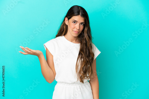 Young caucasian woman isolated on blue background making doubts gesture