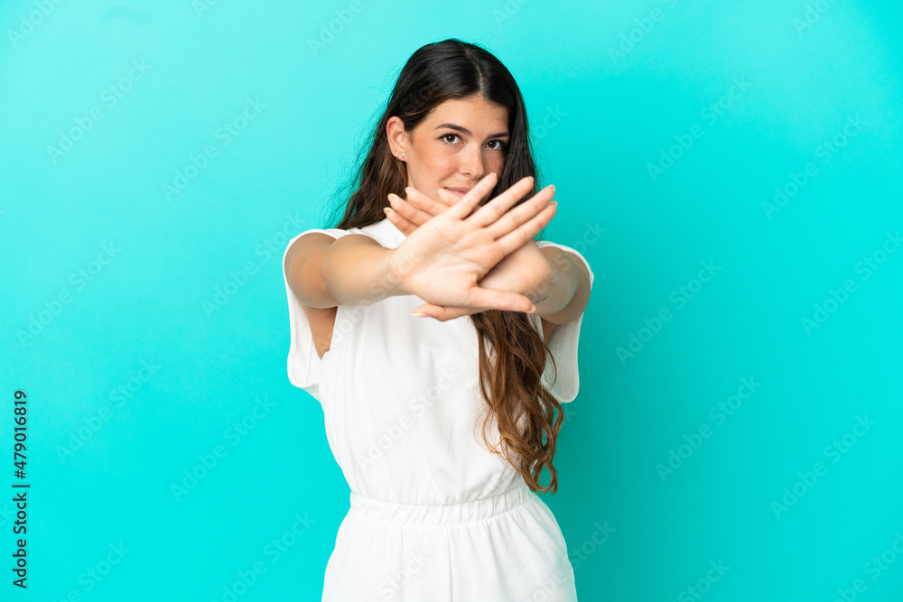 Young caucasian woman isolated on blue background making stop gesture with her hand to stop an act Young caucasian woman isolated on blue background making stop gesture with her hand to stop an act