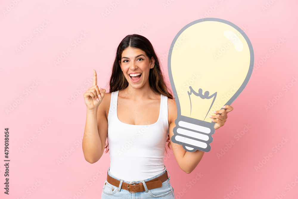 Young caucasian woman isolated on pink background holding a bulb icon and thinking