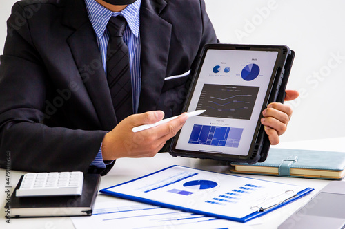 Male accountant calculates last quarter earnings figures and points to tablet to present online documents, business man checking company income and finance documents, modern business man concept.