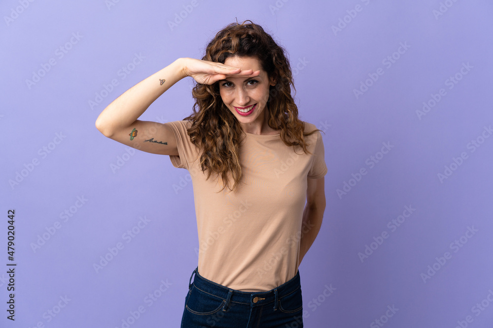 Young caucasian woman isolated on purple background looking far away with hand to look something Young caucasian woman isolated on purple background looking far away with hand to look something