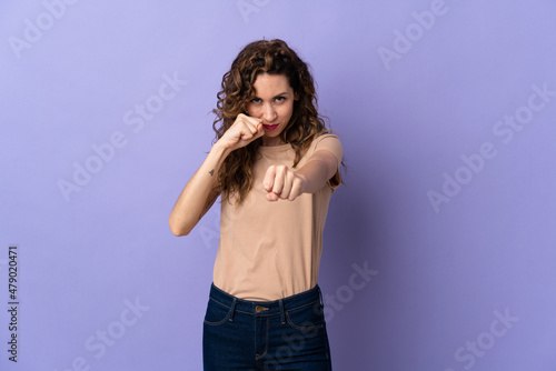 Young caucasian woman isolated on purple background with fighting gesture