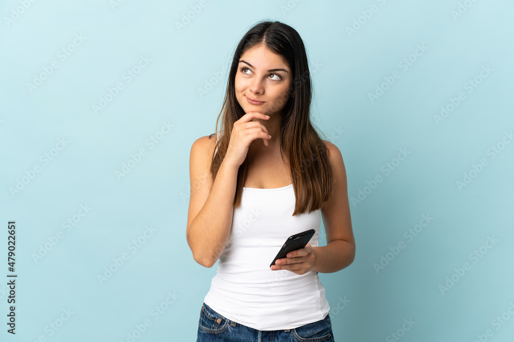 Young caucasian woman using mobile phone isolated on blue background and looking up Young caucasian woman using mobile phone isolated on blue background and looking up