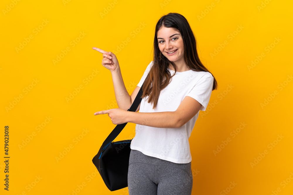 Young sport woman with sport bag isolated on yellow background pointing finger to the side and presenting a product Young sport woman with sport bag isolated on yellow background pointing finger to the side and presenting a product