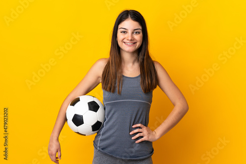 Young football player woman isolated on yellow background posing with arms at hip and smiling © luismolinero