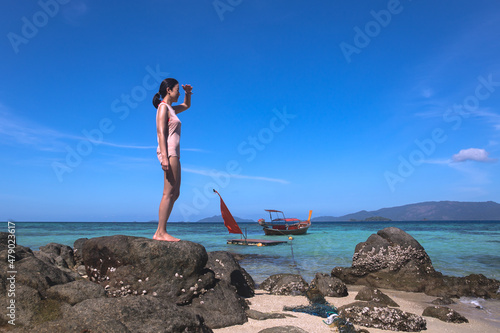 Beautiful woman standing on the beach rock looking over the ocean.