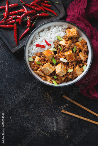 Bowl of chinese mapo tofu with rice over dark-brown stone background, vertical shot with space, view from above