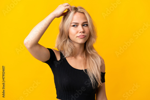 Young Russian woman isolated on yellow background having doubts while scratching head