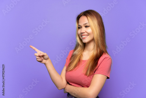 Teenager girl over isolated purple background pointing finger to the side