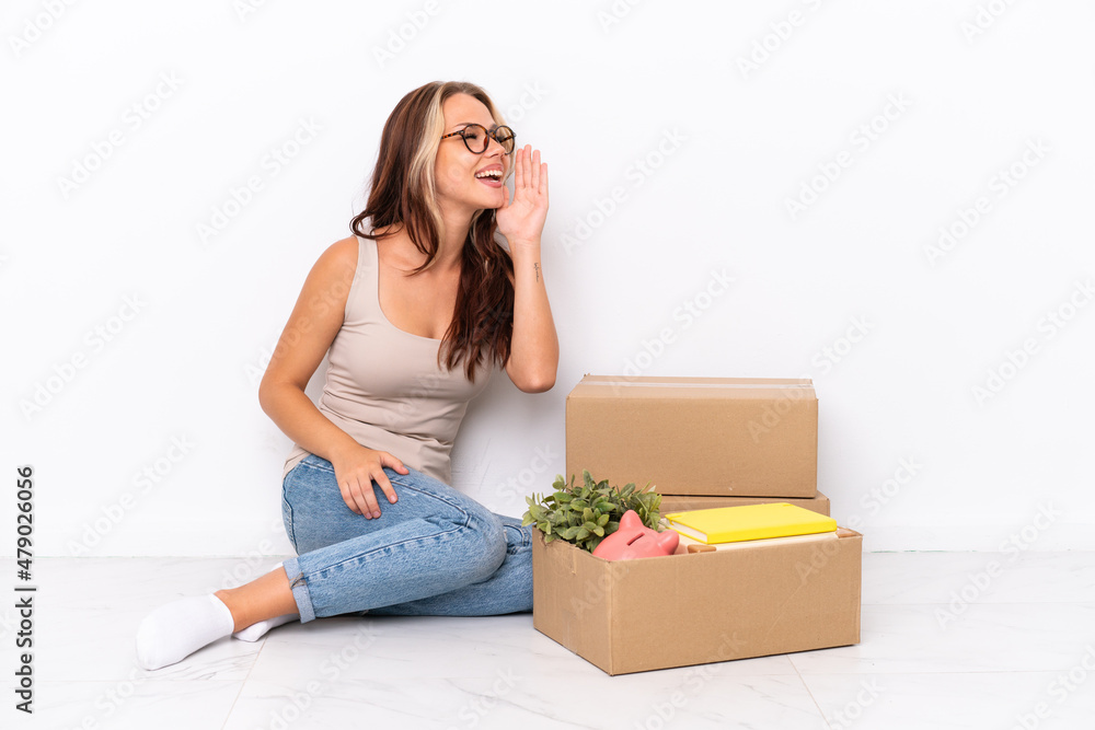 Young Russian girl sitting on the floor isolated on white background shouting with mouth wide open to the lateral Young Russian girl sitting on the floor isolated on white background shouting with mouth wide open to the lateral