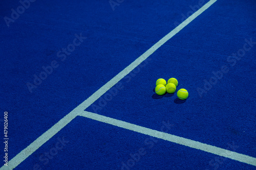 Multiple balls next to the lines of a blue paddle tennis court. © Vic
