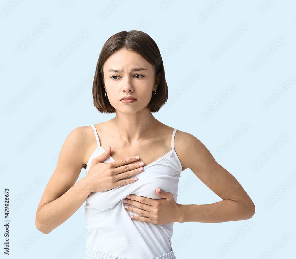 Young woman feeling discomfort in her breast on light background. Cancer awareness concept Young woman feeling discomfort in her breast on light background. Cancer awareness concept