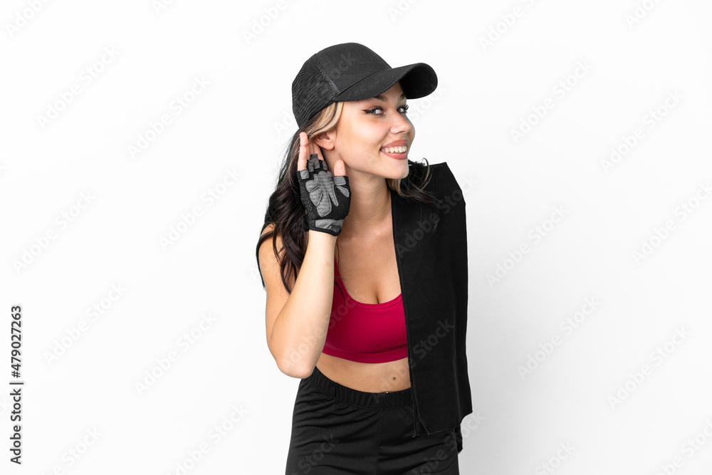 Sport Russian girl with hat and towel isolated on white background listening to something by putting hand on the ear Sport Russian girl with hat and towel isolated on white background listening to something by putting hand on the ear