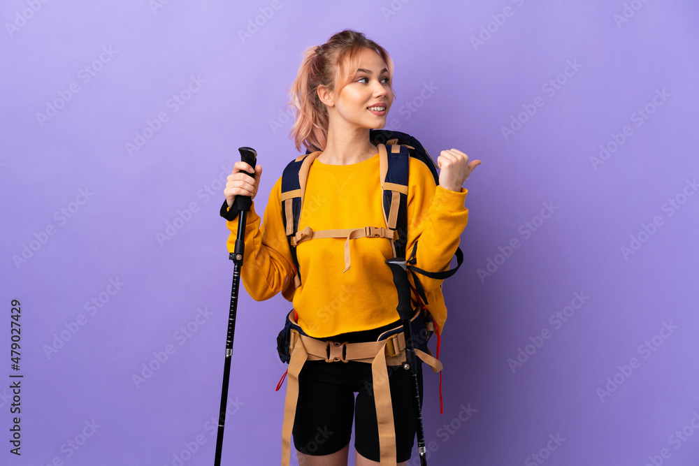 Teenager girl with backpack and trekking poles over isolated purple background pointing to the side to present a product