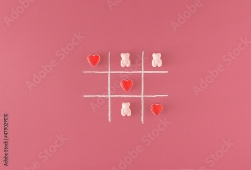 Tic tac toe game with a white chalk and gummy candies on a pink background. Minimal concept.
