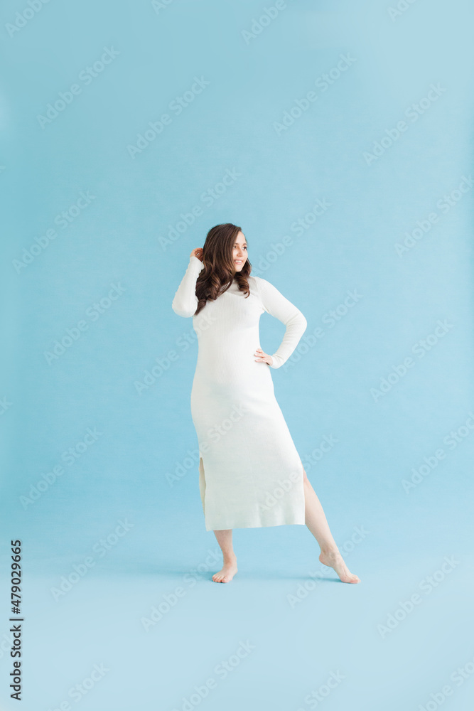 Pretty pregnant woman in white cotton dress standing on blue background Pretty pregnant woman in white cotton dress standing on blue background