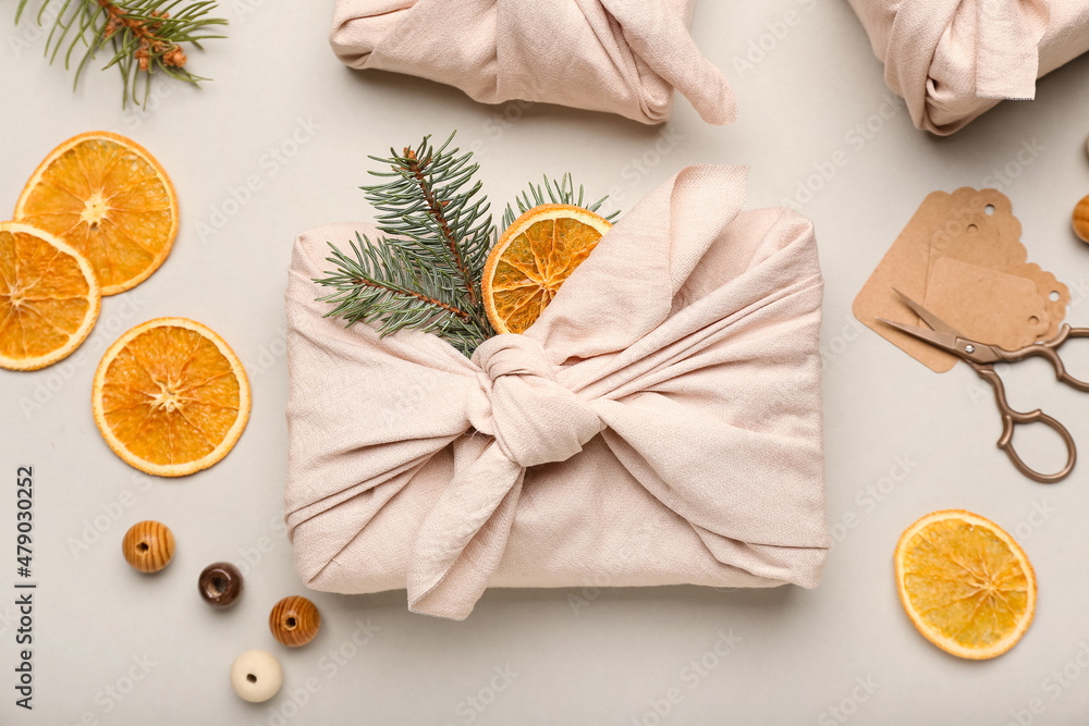 Obraz premium Beautiful Christmas gift wrapped in fabric on light background