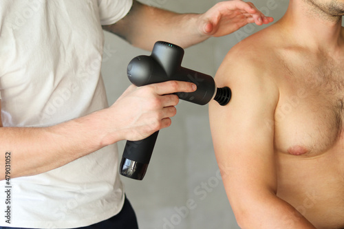 Therapist massaging mans hand with massage percussion device after workout. Sports gun percussion massage in medical room