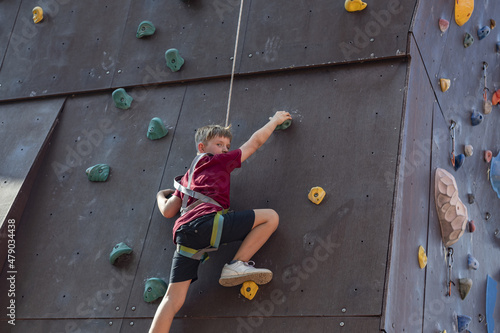 A boy climbs the top of a climbing wall in a sports park climbing wall.