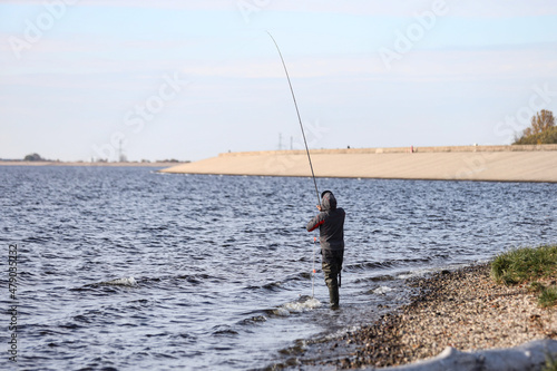 Fisherman standing with back to camera and facing water.