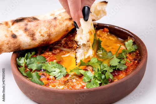 shakshuka with herbs, cheese and fresh pastries on a light background