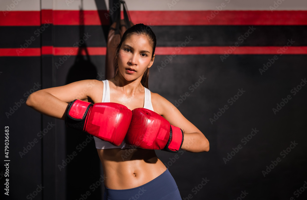 Portrait of confident Asian woman in sportswear wear red boxing gloves with workout and pose boxing show punch in gym.