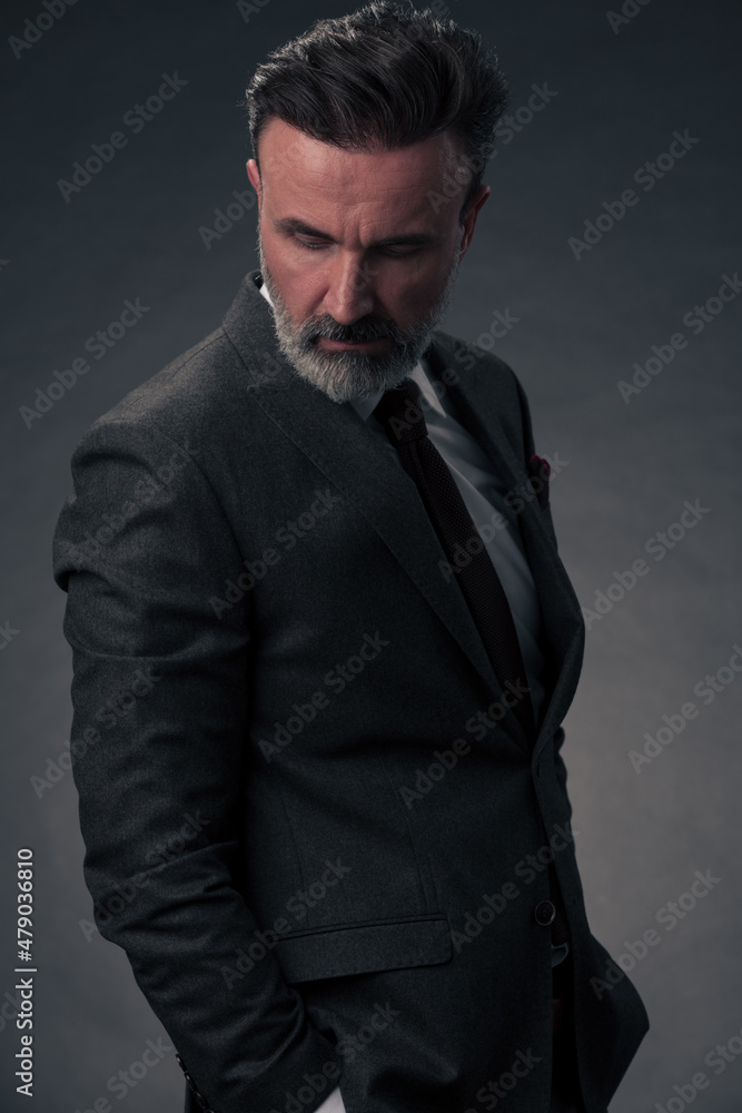 Portrait of a stylish elegant senior businessman with a beard and casual business clothes in photo studio isolated on dark background gesturing with hands