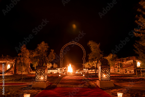 Glowing lanterns beside carpet on sand in sahara desert during night, Illuminated lanterns with ornamental pattern on sand photo