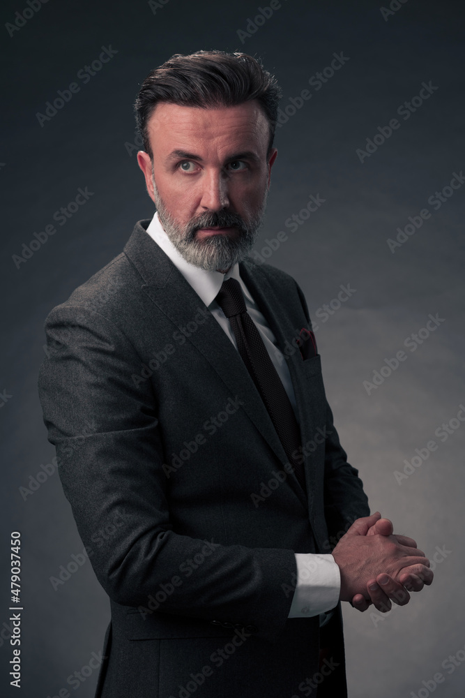 Portrait of a stylish elegant senior businessman with a beard and casual business clothes in photo studio isolated on dark background gesturing with hands Portrait of a stylish elegant senior businessman with a beard and casual business clothes in photo studio isolated on dark background gesturing with hands