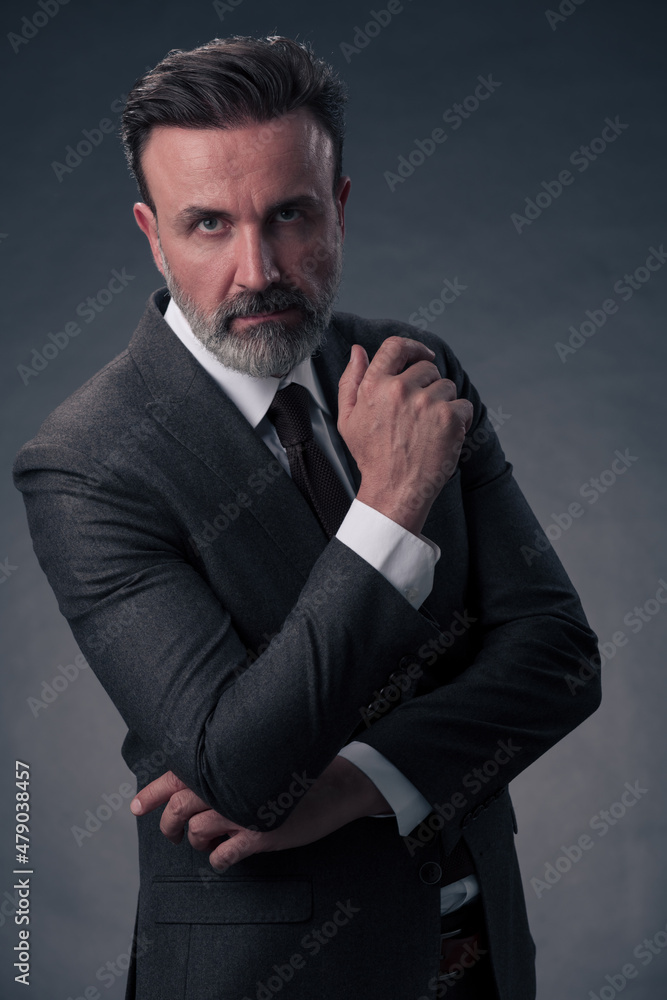 Portrait of a stylish elegant senior businessman with a beard and casual business clothes in photo studio isolated on dark background gesturing with hands Portrait of a stylish elegant senior businessman with a beard and casual business clothes in photo studio isolated on dark background gesturing with hands