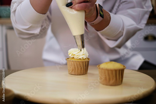 Women in pastry bakery as confectioner glazing muffins with icing bag, close-up photo