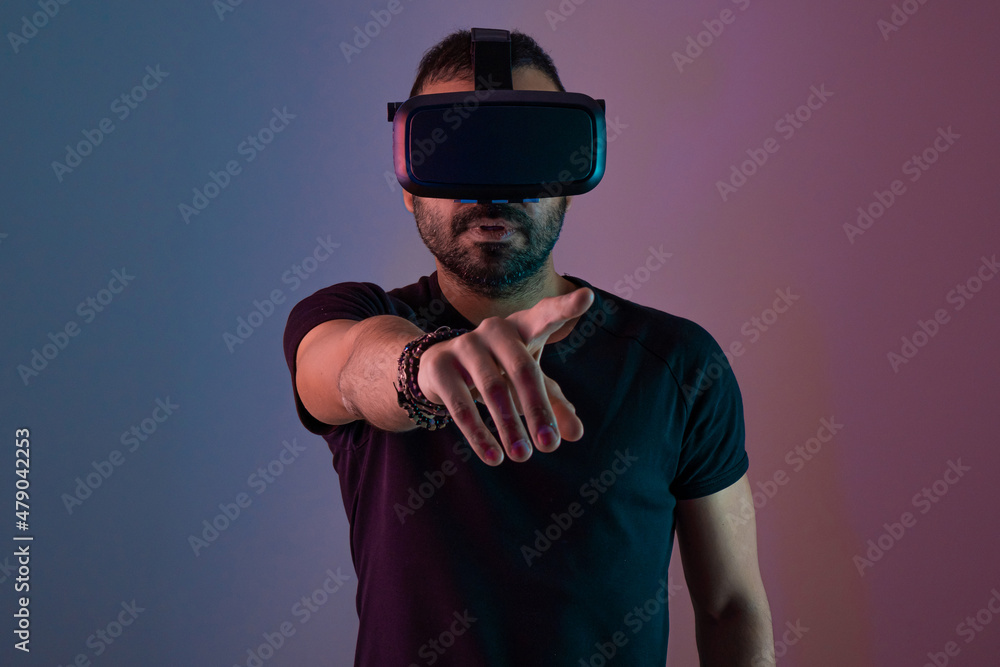 Young man in VR glasses headset interact with virtual reality in color neon light, future technology, education video gaming Young man in VR glasses headset interact with virtual reality in color neon light, future technology, education video gaming