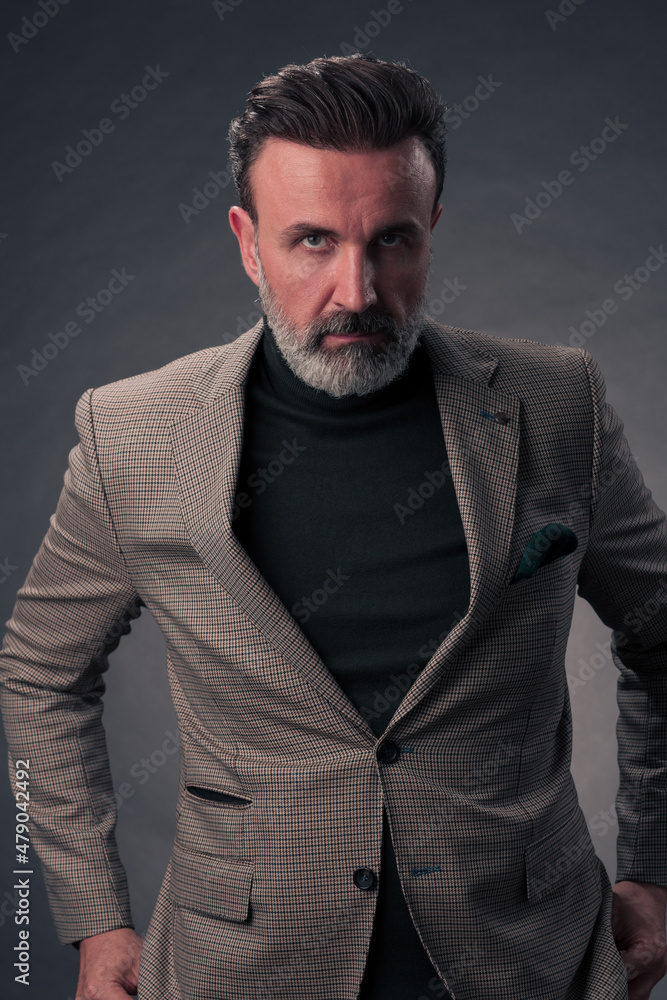 Portrait of a stylish elegant senior businessman with a beard and casual business clothes in photo studio isolated on dark background gesturing with hands