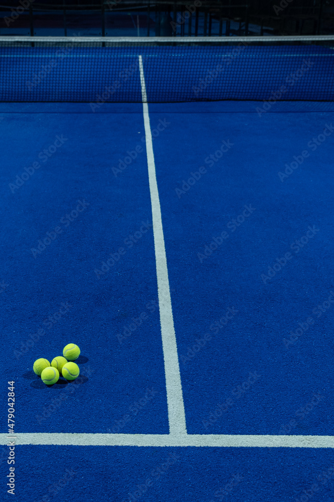 Several balls on a blue paddle tennis court in the evening