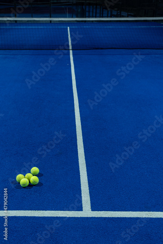 Several balls on a blue paddle tennis court in the evening