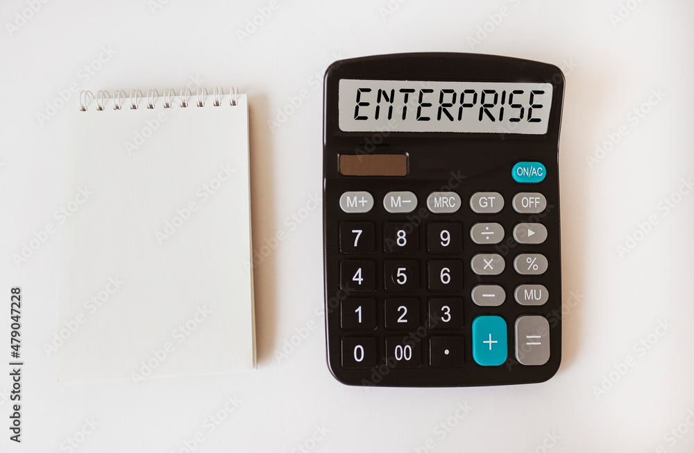 The word Enterprise on the display of the calculator. Near a notepad for writing on a white background The word Enterprise on the display of the calculator. Near a notepad for writing on a white background