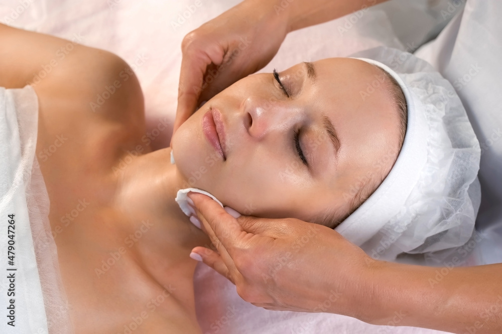 Cosmetologist doctor wiping woman's face and neck using cotton pads. Doctor is making beauty procedure in cosmetology clinic. Beautician cleaning patient's face in beauty clinic.