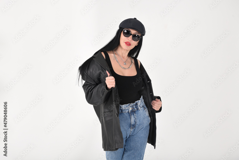 A gorgeous brunette in the studio on a white background wearing sunglasses, a black cap and a black leather jacket, jeans with chains around her neck A gorgeous brunette in the studio on a white background wearing sunglasses, a black cap and a black leather jacket, jeans with chains around her neck