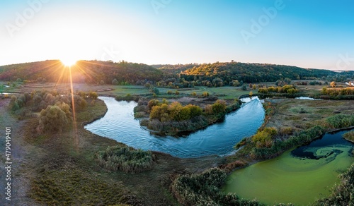 Hill slopes surround green meadows and river at sunset